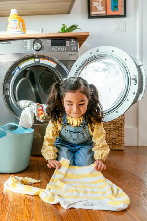 Girl folding laundry on floor in front of dryer