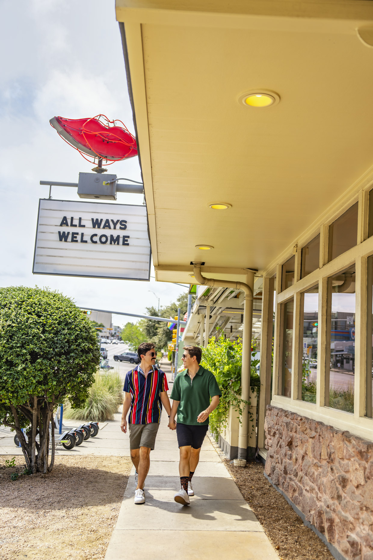 Male Couple Walking outside on sidewalk underneath sign