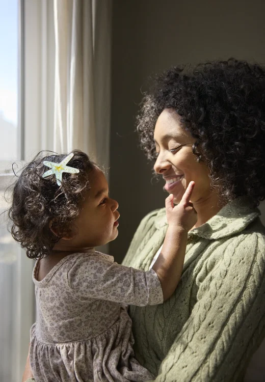 Daughter touches mom's face by sunlit window