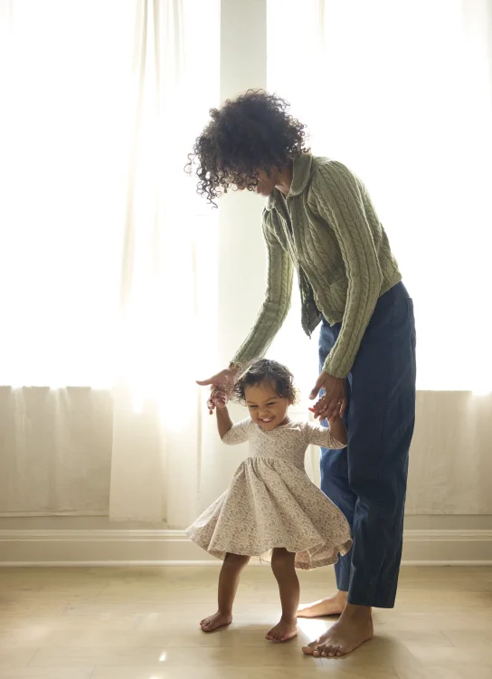 Mom holds daughter's hands while she twirls her in her dress