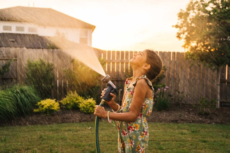 Girl Plays with Garden Hose in Backyard